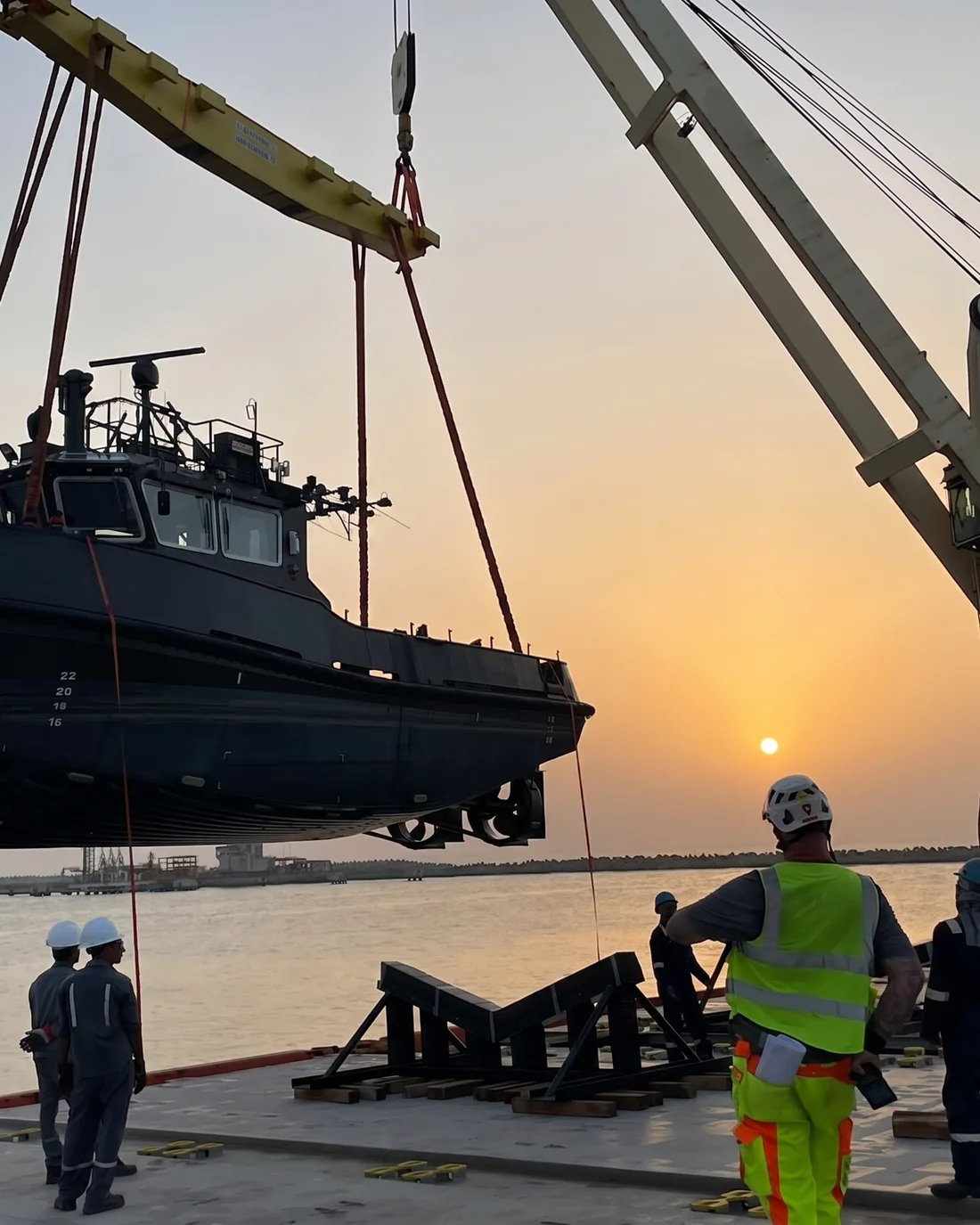 A vessel being lifted by crane at a UAE port at sunset